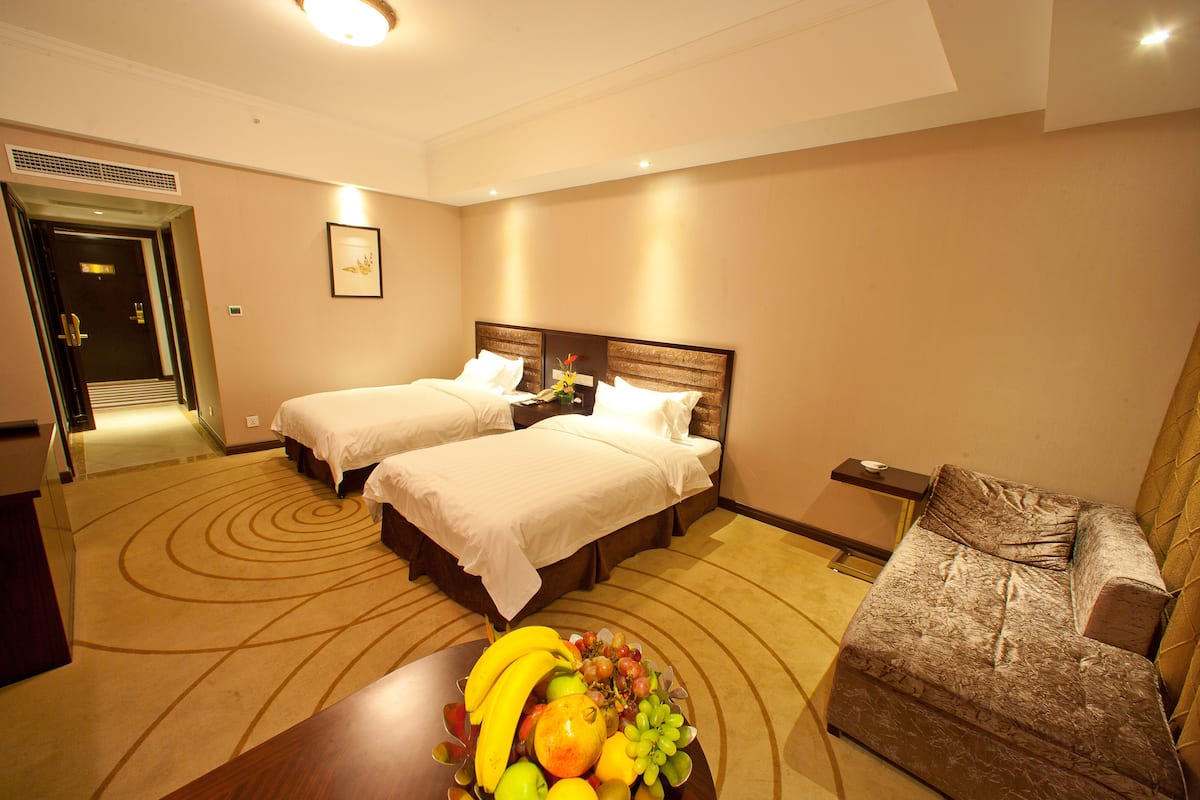 Une chambre d’hôtel avec deux lits, un canapé, un panier de fruits et une petite table.