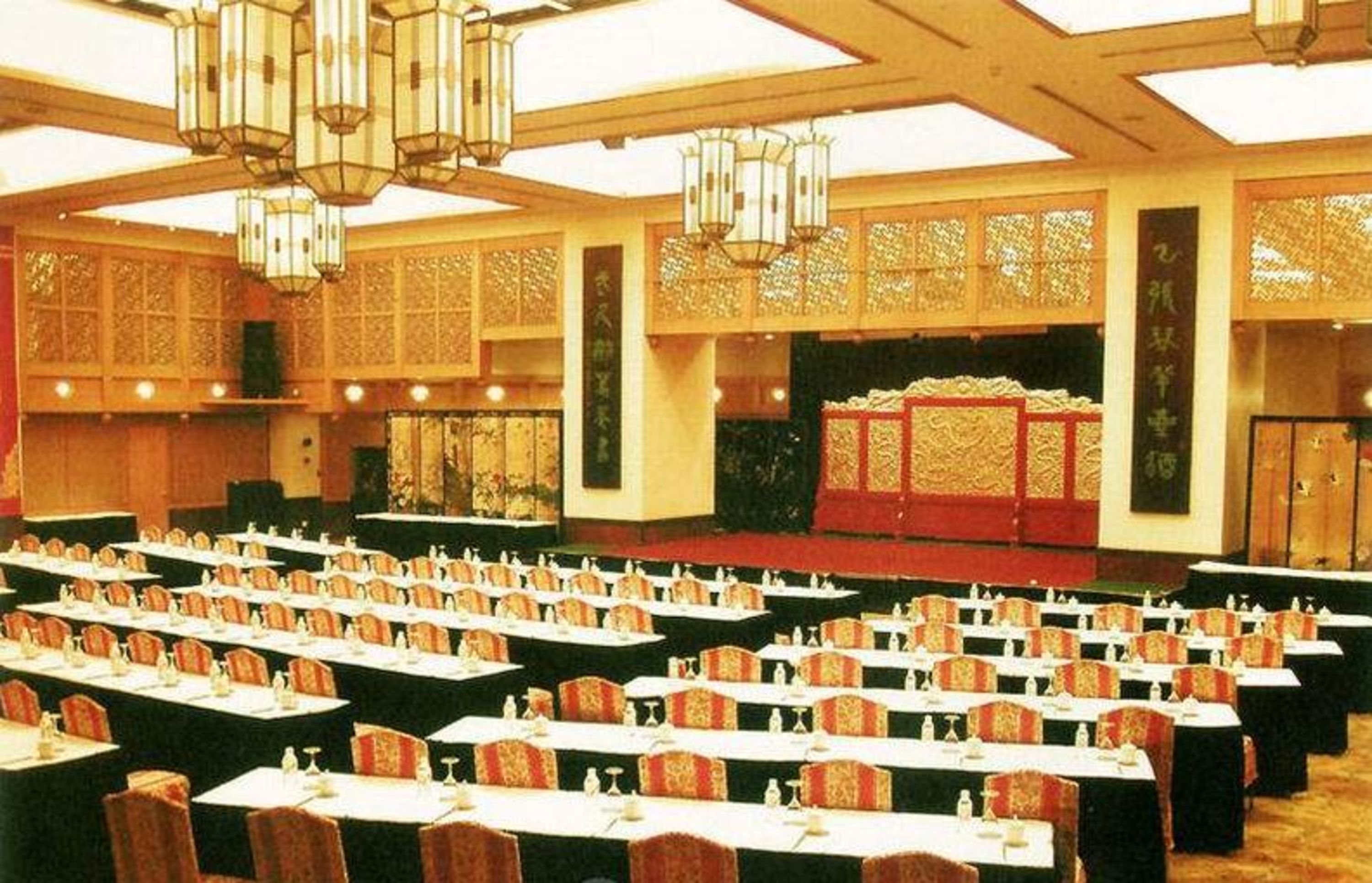 A banquet hall with rows of tables and chairs, decorative lanterns, and traditional Asian-style wall panels.