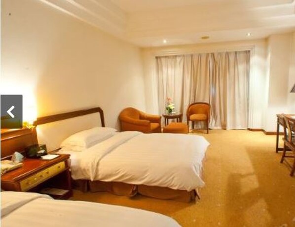 A hotel room with two beds, a desk, a chair, and a window with curtains.