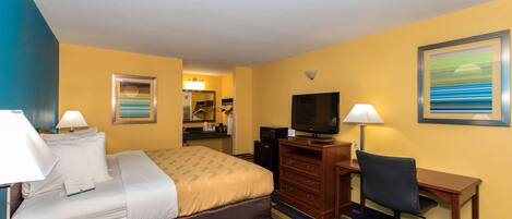 A hotel room with a bed, desk, chair, television, and a bathroom visible in the background.