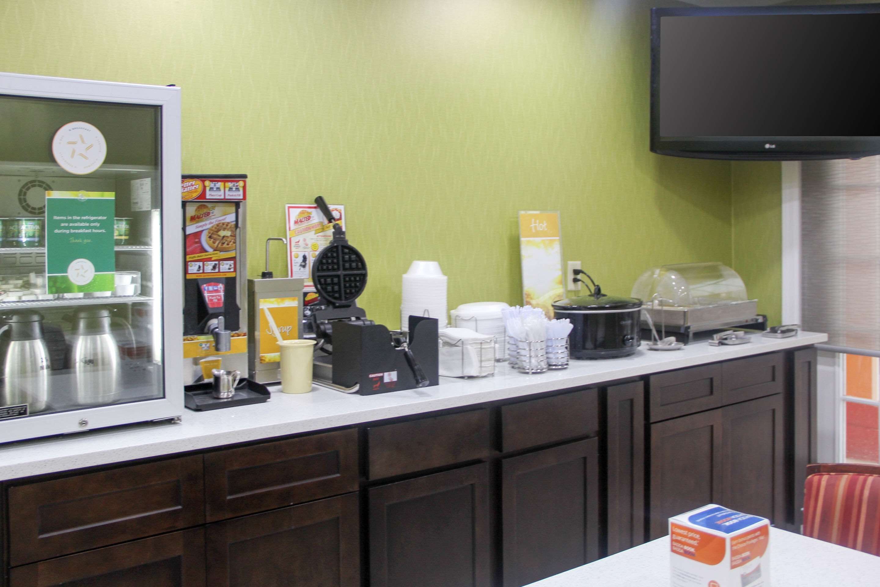 A breakfast bar with a coffee machine, waffle maker, and various food items.
