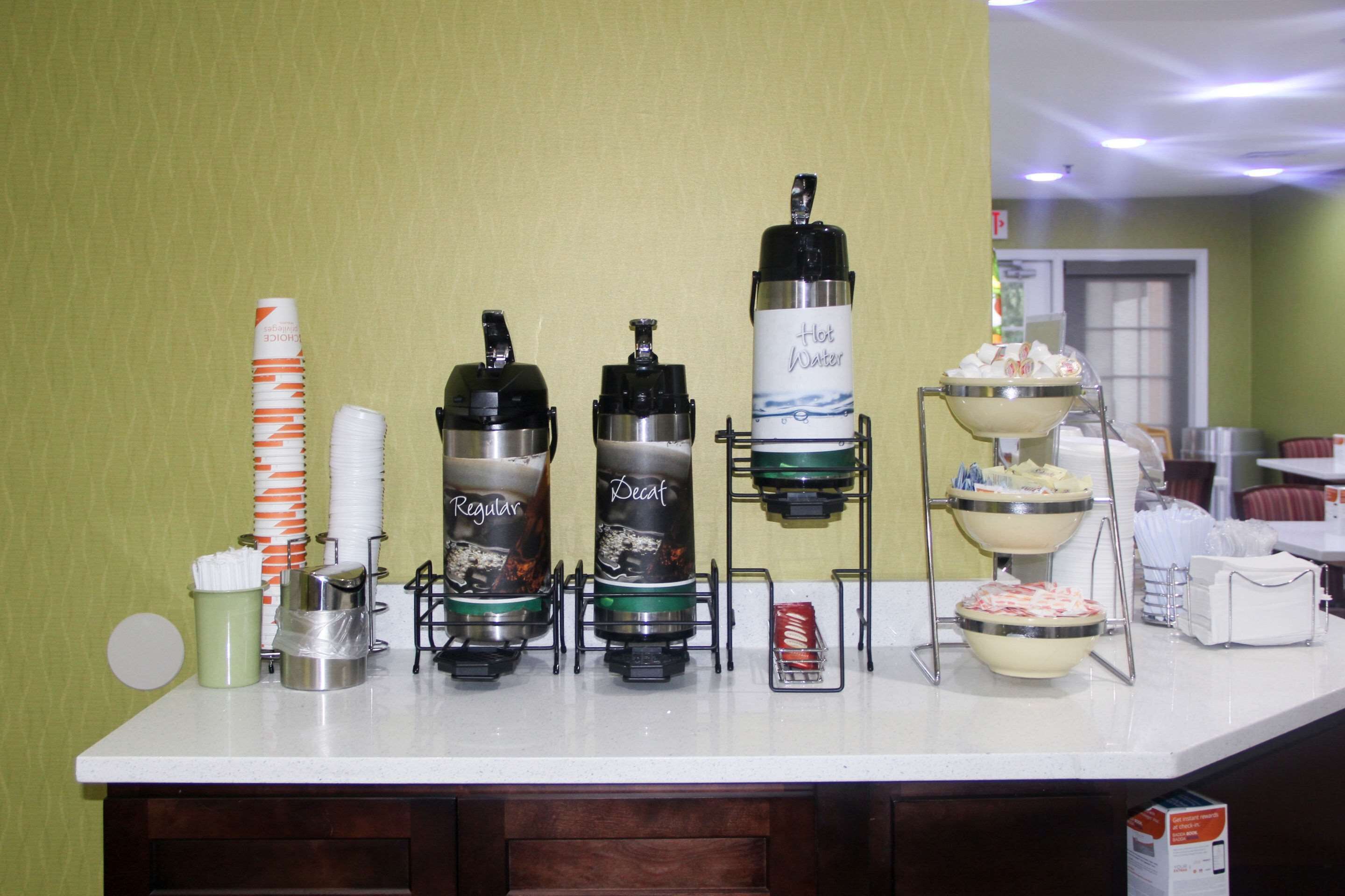 Montaje de bufé con varios dispensadores de bebidas etiquetados como 'Regular' y 'Descafeinado', un dispensador de 'Agua Caliente' y un tazón de comida.