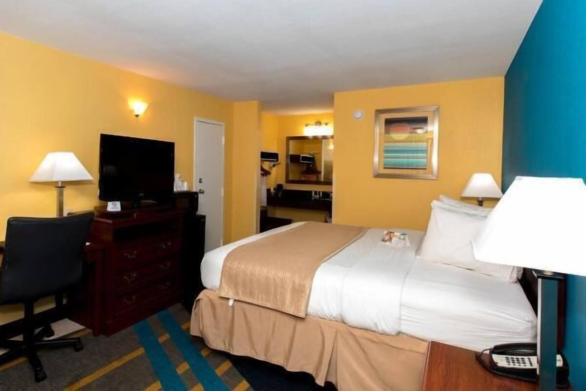 A hotel room with a bed, desk, chair, television, and a bathroom visible in the background.