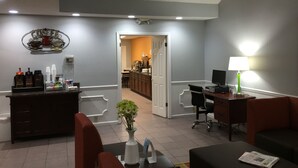 A hotel lobby with a reception desk, seating area, and a kitchenette in the background.