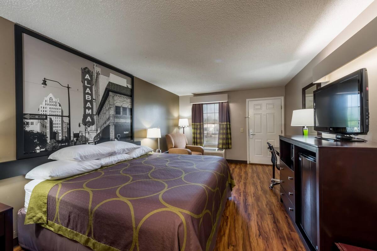 A hotel room with a large bed, a television, a desk, and a window with curtains.