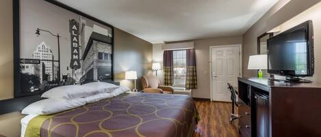 A hotel room with a large bed, a television, a desk, and a window with curtains.