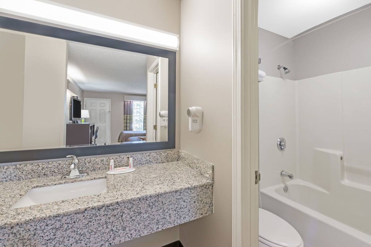 A bathroom with a granite countertop sink, a large mirror, a toilet, and a shower.