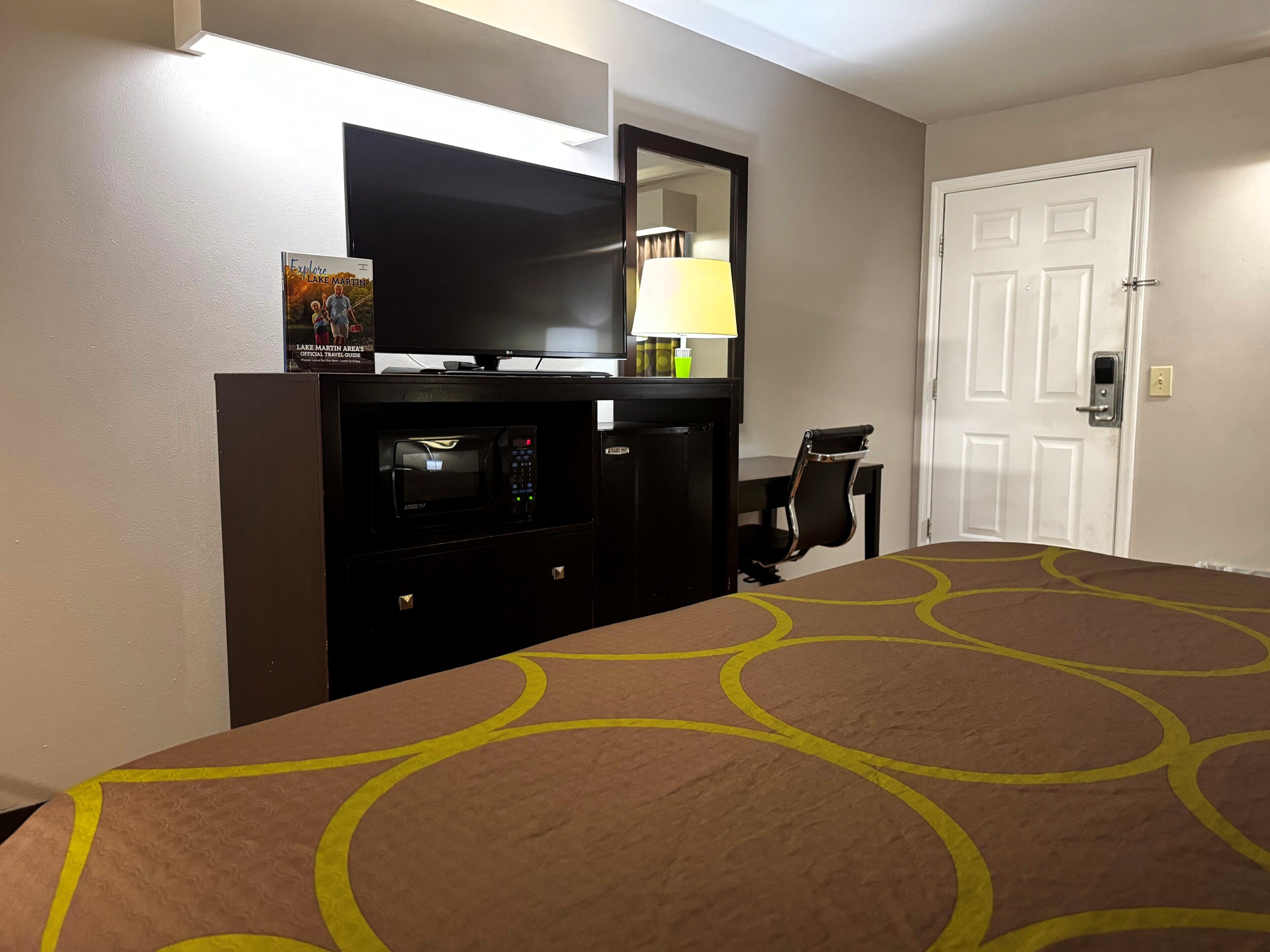 Habitación de hotel con cama, escritorio, microondas, televisor y puerta.