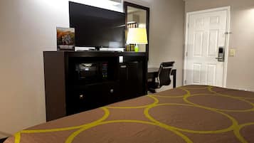 Habitación de hotel con cama, escritorio, microondas, televisor y puerta.