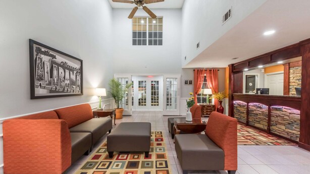 A spacious lobby with a high ceiling, a ceiling fan, a large framed welcome sign, and a reception desk with a stone accent wall.