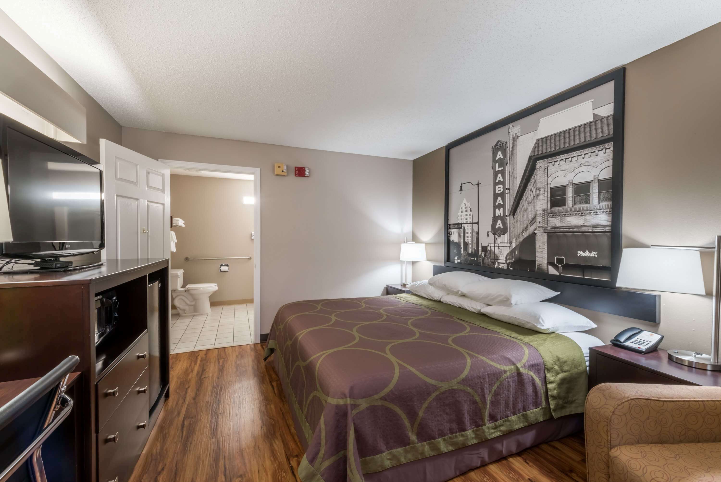 A hotel room with a bed, a desk, a TV, and a bathroom visible through an open door.