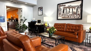 A hotel lobby with leather sofas, a coffee table, a desk with a computer, a water dispenser, and a framed welcome sign.