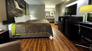 A hotel room with a bed, a desk with a computer, a TV, and a large painting on the wall.