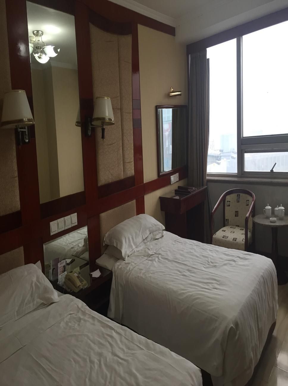 Een hotelkamer met twee bedden, een bureau, een stoel, een spiegel en een raam met uitzicht.