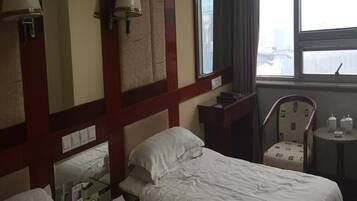 Een hotelkamer met twee bedden, een bureau, een stoel, een spiegel en een raam met uitzicht.
