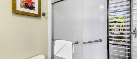Un baño con inodoro, un perchero con toalla blanca, ducha con puerta de cristal y un cuadro en la pared.