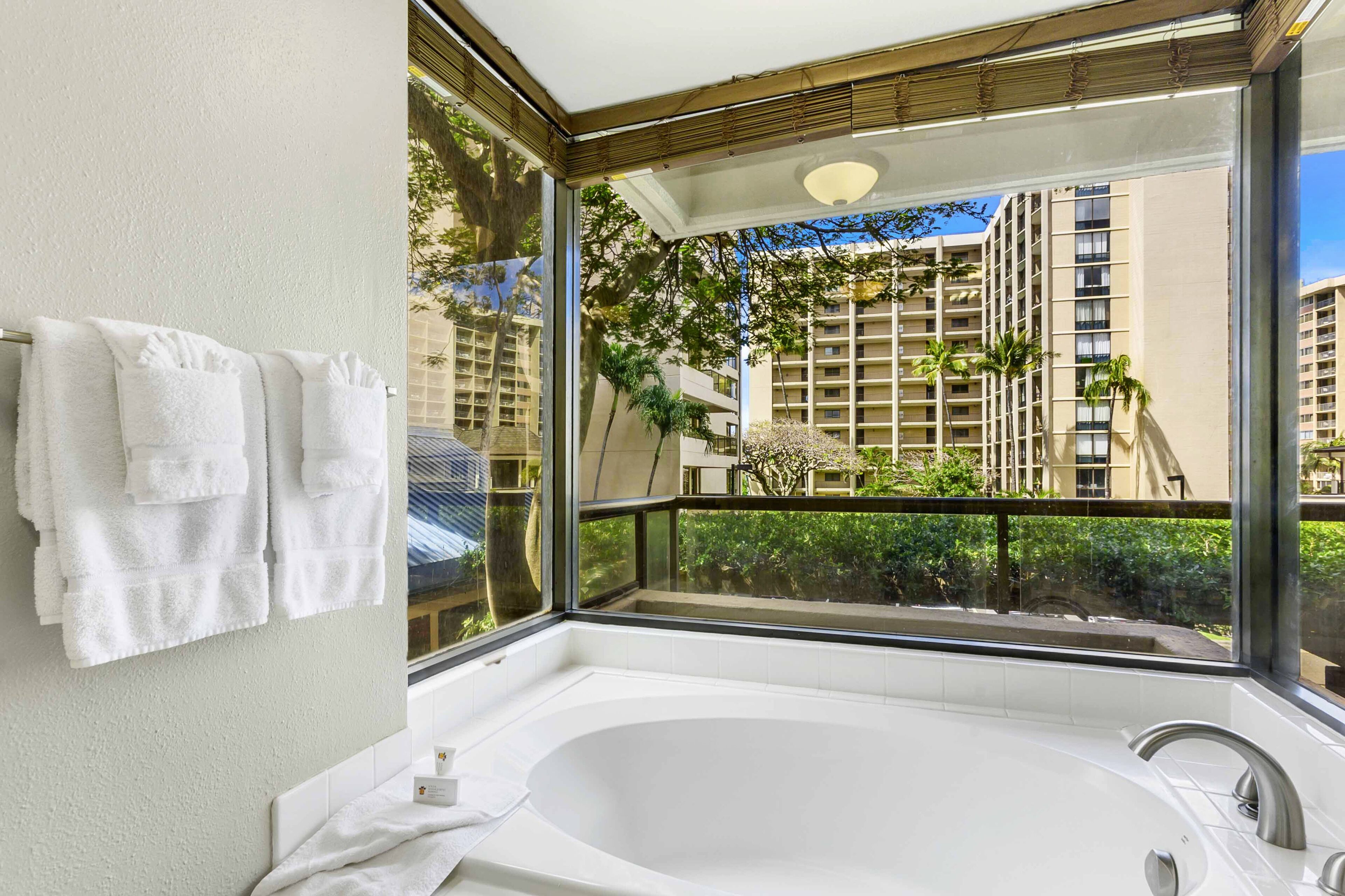 A modern bathroom with a large bathtub, a glass-enclosed balcony, and a view of high-rise buildings.