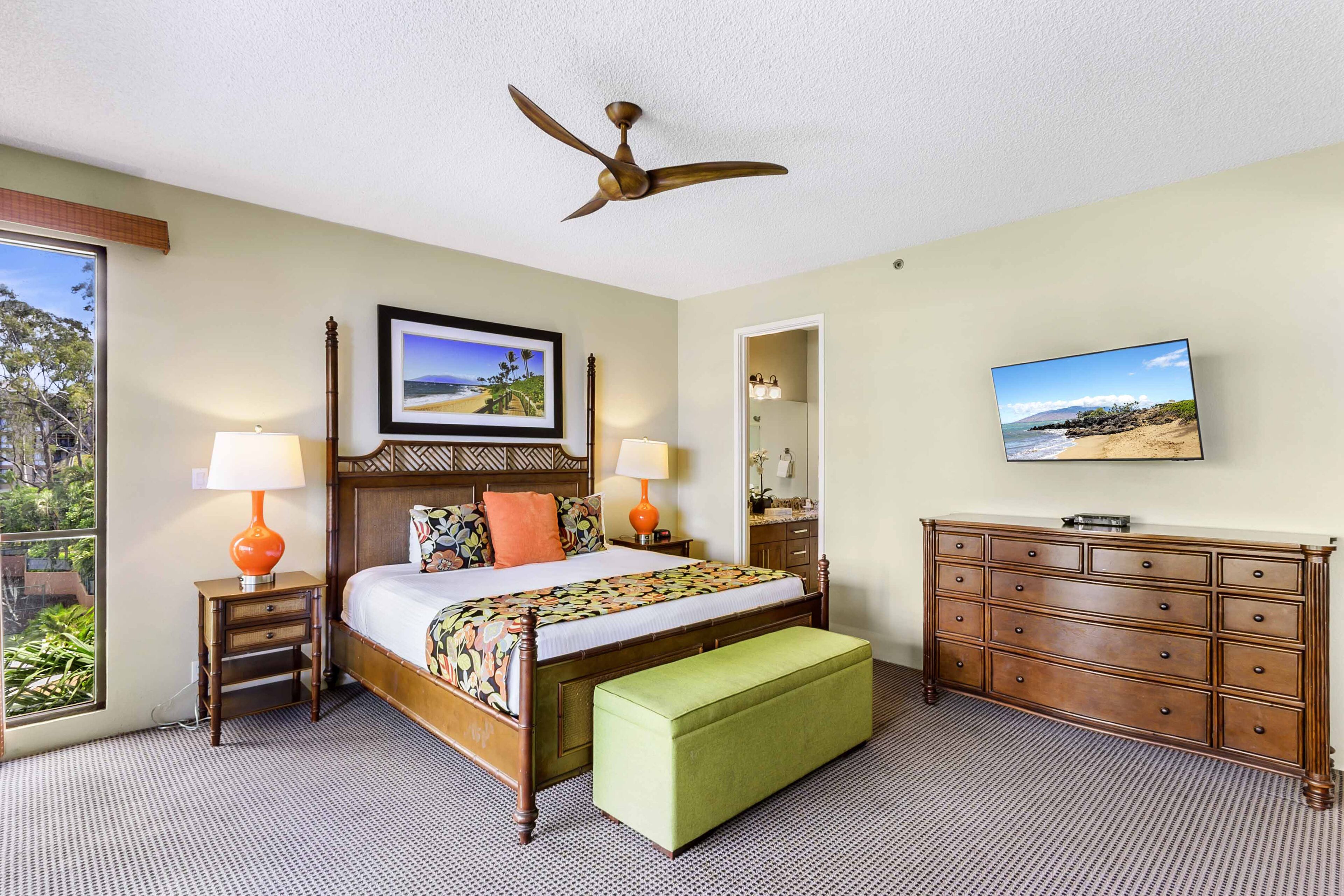 A hotel room with a bed, a green bench, a dresser, a ceiling fan, and two lamps.