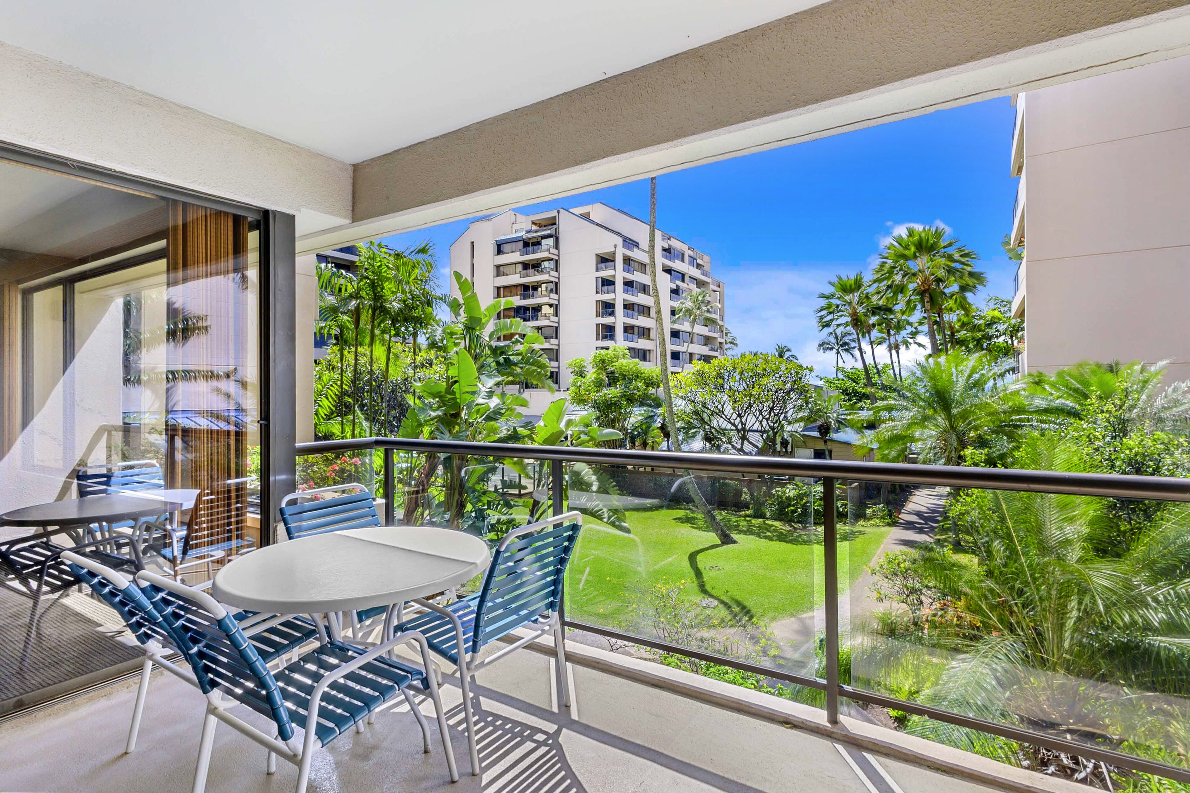 A balcony with a table and chairs, overlooking a lush garden and a building.