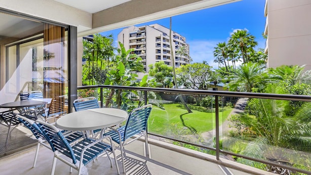 Un balcón con mesa y sillas, con vistas a un jardín exuberante y un edificio.