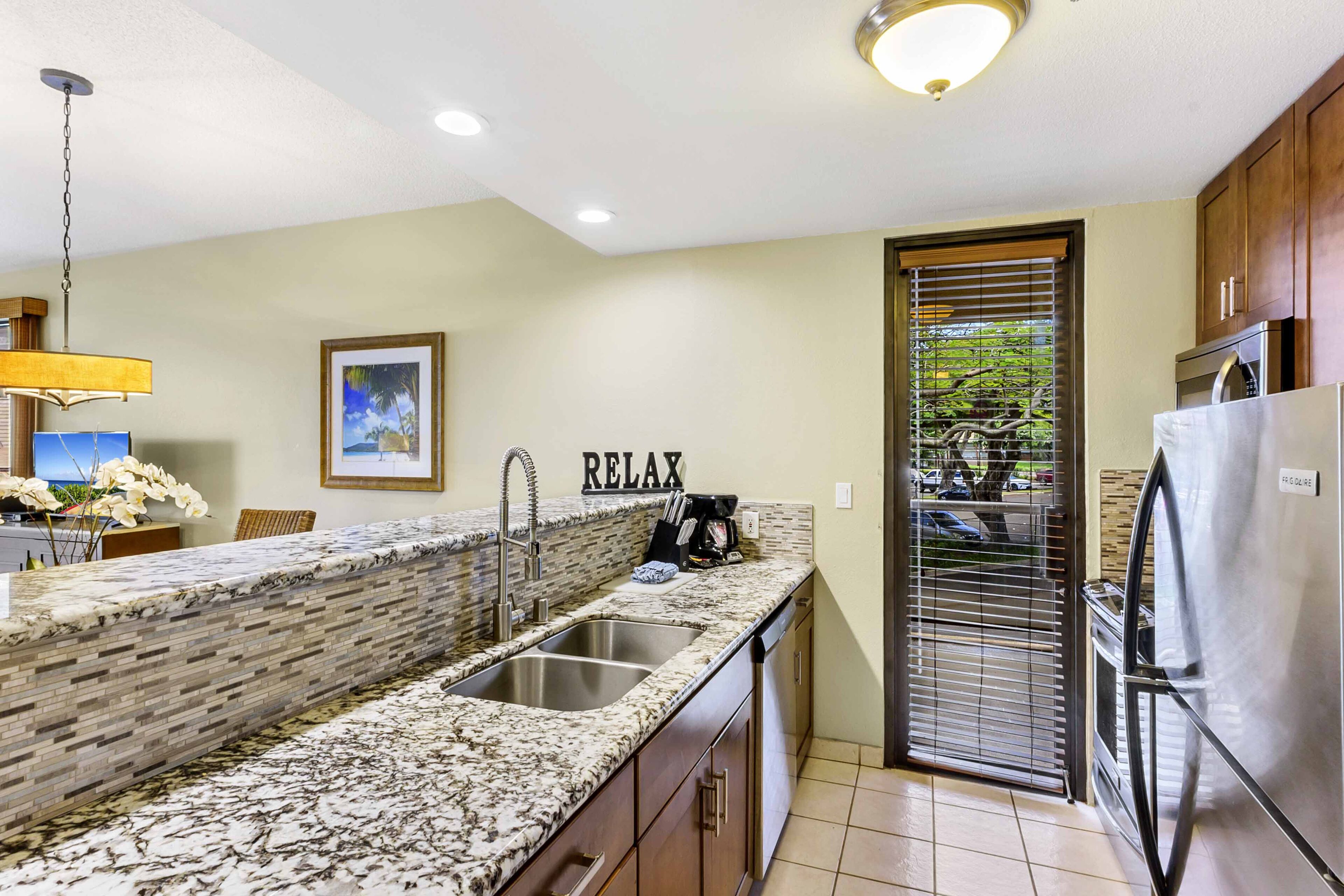 A kitchen with a granite countertop, stainless steel appliances, and a 'RELAX' sign on the wall.