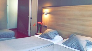 A hotel room with two beds, a nightstand with a vase of red tulips, and a wall-mounted light.