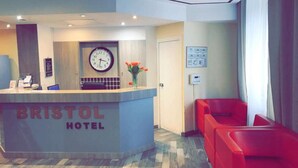 A reception desk with a clock, a vase with flowers, and a red seating area. - Bristol République (Paris)