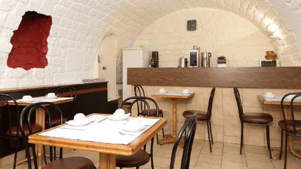 A restaurant with a rustic brick archway, wooden tables, and black chairs.