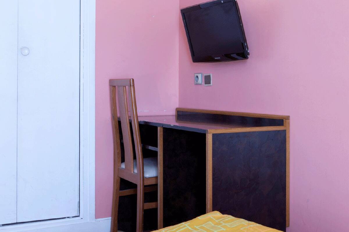 Une chambre avec un lit, un bureau, une chaise et un téléviseur fixé au mur.