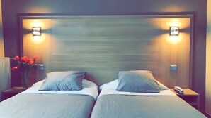 A hotel room with two beds, a nightstand with a phone, and a wall-mounted light fixture. - Bristol République (Paris)