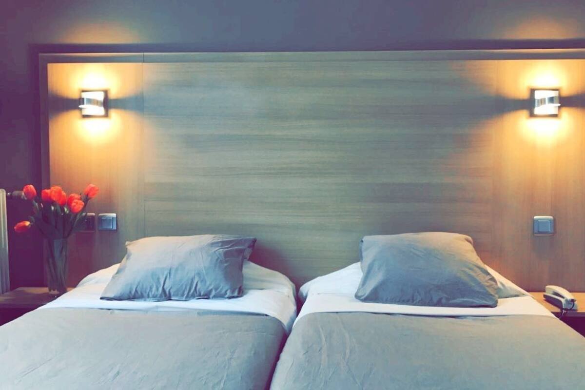 Une chambre d’hôtel avec deux lits, une table de chevet avec un téléphone et un luminaire fixé au mur.