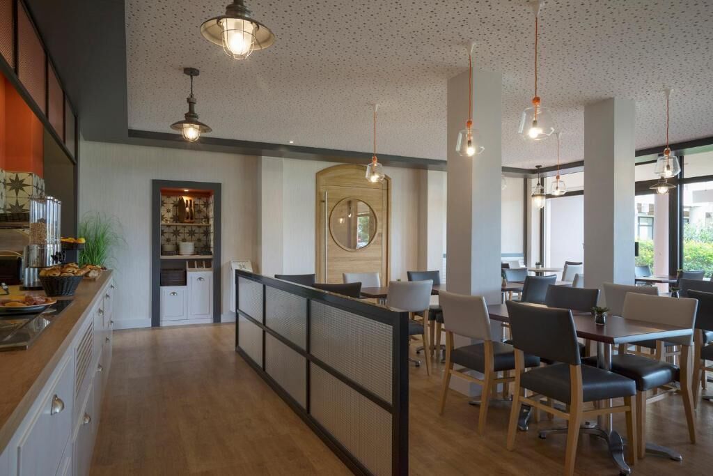 Un comedor moderno con mesas y sillas altas, iluminación colgante y vistas al exterior.