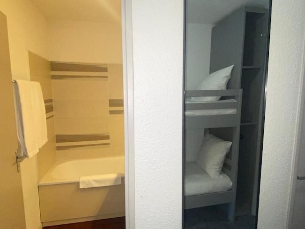 A small, compact room with a single bed, a built-in bench, and a shower area.