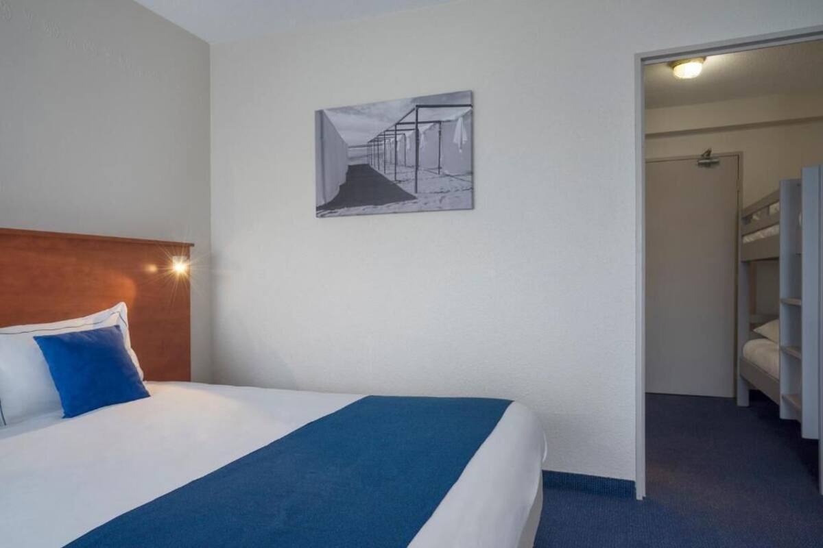 Une chambre d’hôtel avec un lit, une tête de lit, une œuvre d’art accrochée au mur et une vue sur la chambre voisine.