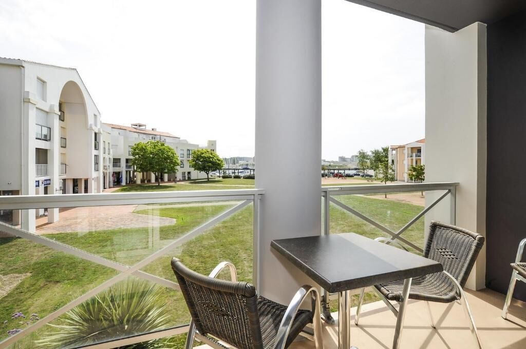 Un balcón con mesa y sillas, con vistas a un patio con edificios y árboles.