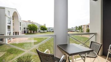 Un balcón con mesa y sillas, con vistas a un patio con edificios y árboles.