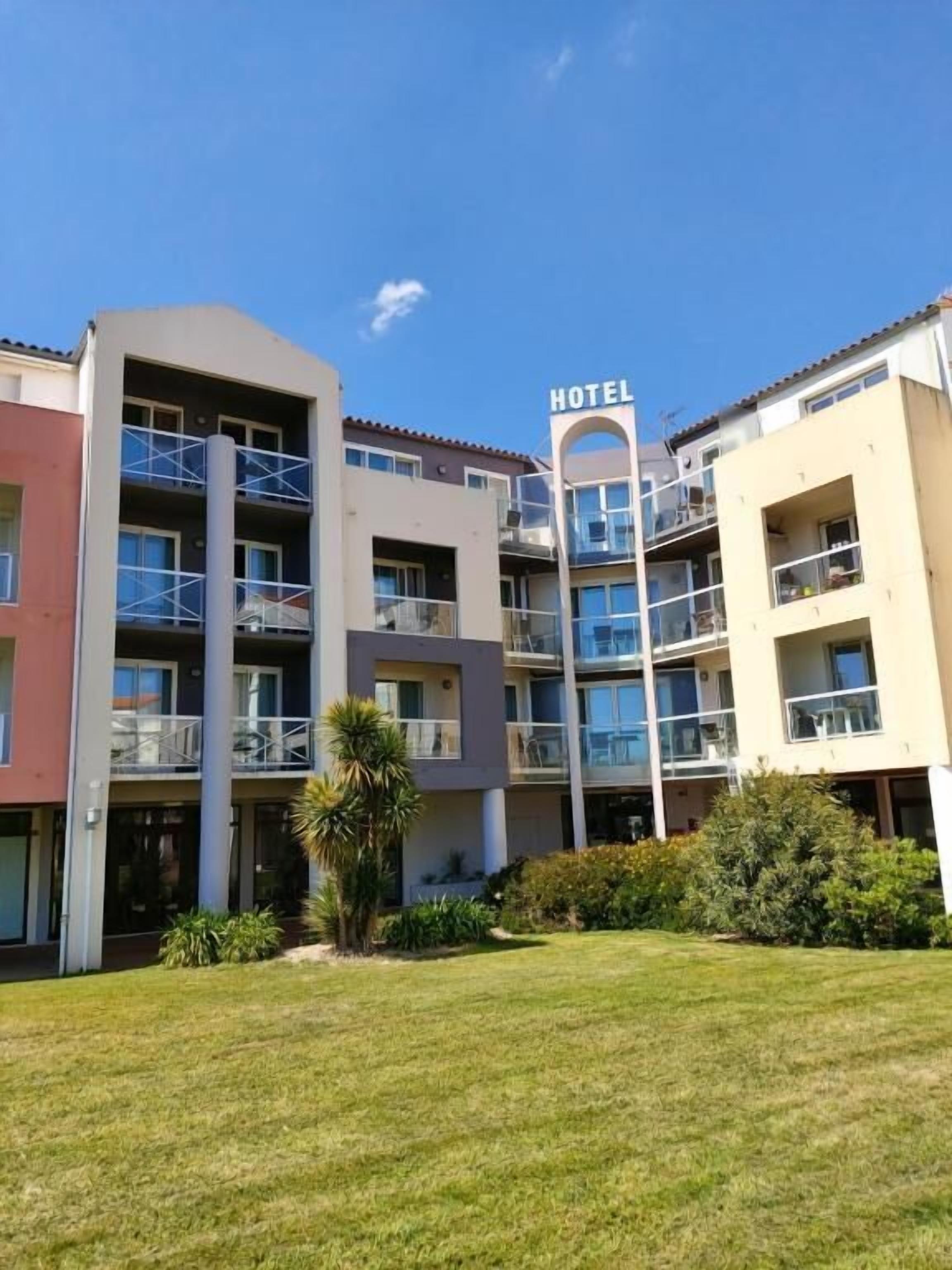 Een meerhoog hotelgebouw met balkons, een bord dat aangeeft dat het een hotel is, en een verzorgd gazon ervoor.