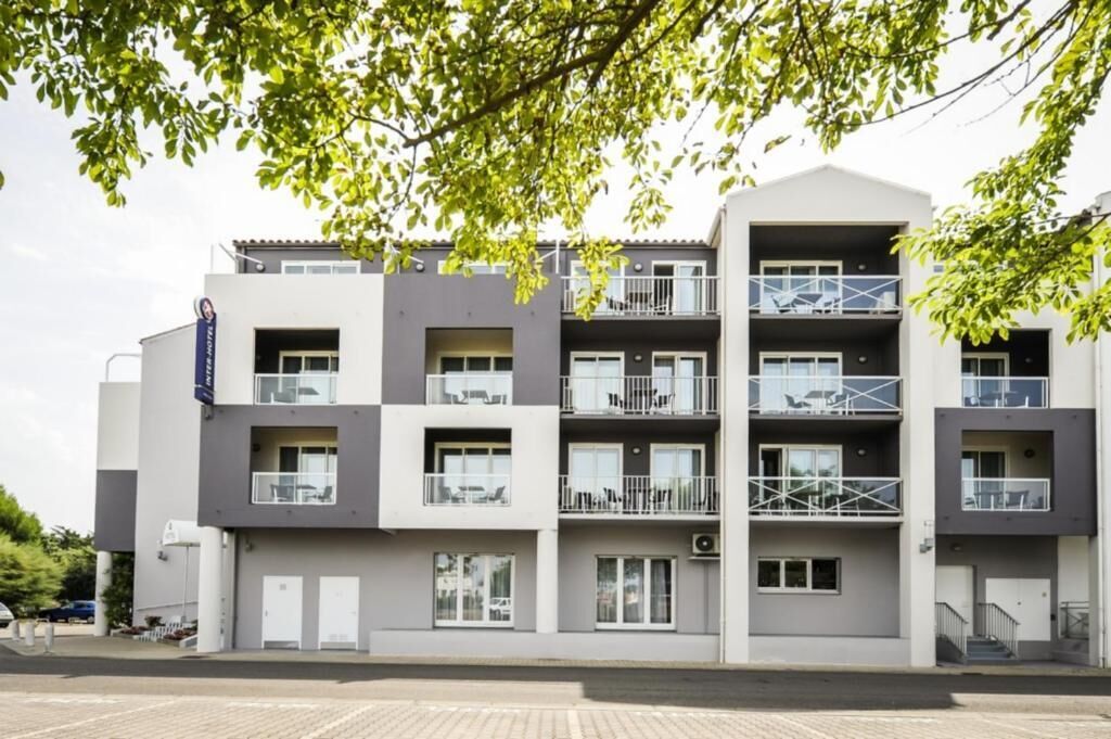 Un immeuble à plusieurs étages doté de balcons, d’un parking et d’une enseigne indiquant qu’il s’agit d’un hôtel.