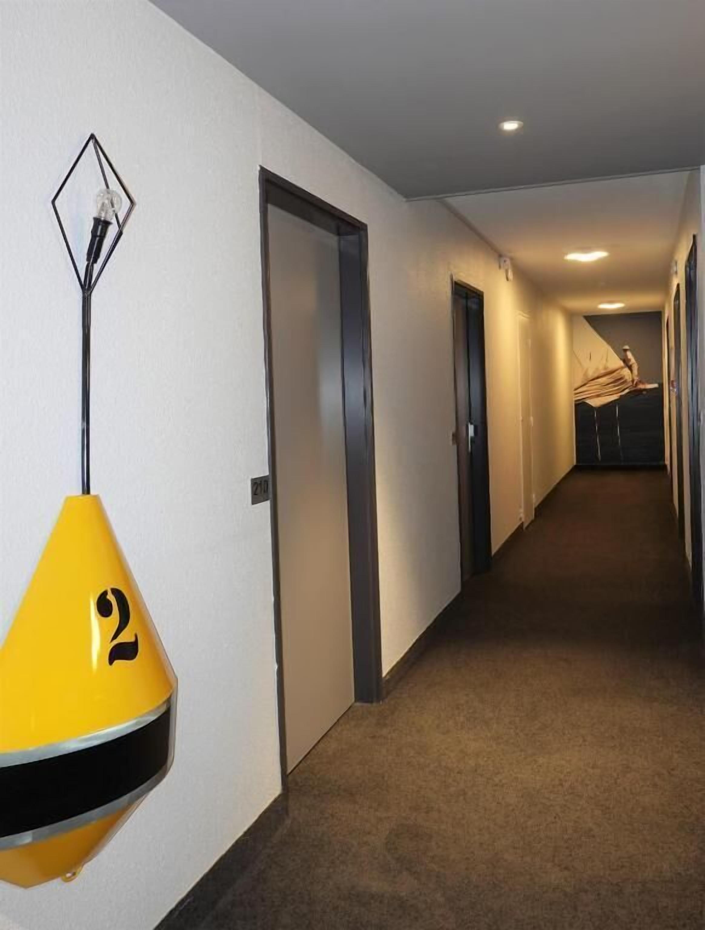 Un pasillo de hotel con una lámpara colgante amarilla, puertas y suelo alfombrado.