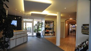 Een hotellobby met een receptiebalie, een grote plant en een presentatie van spullen.