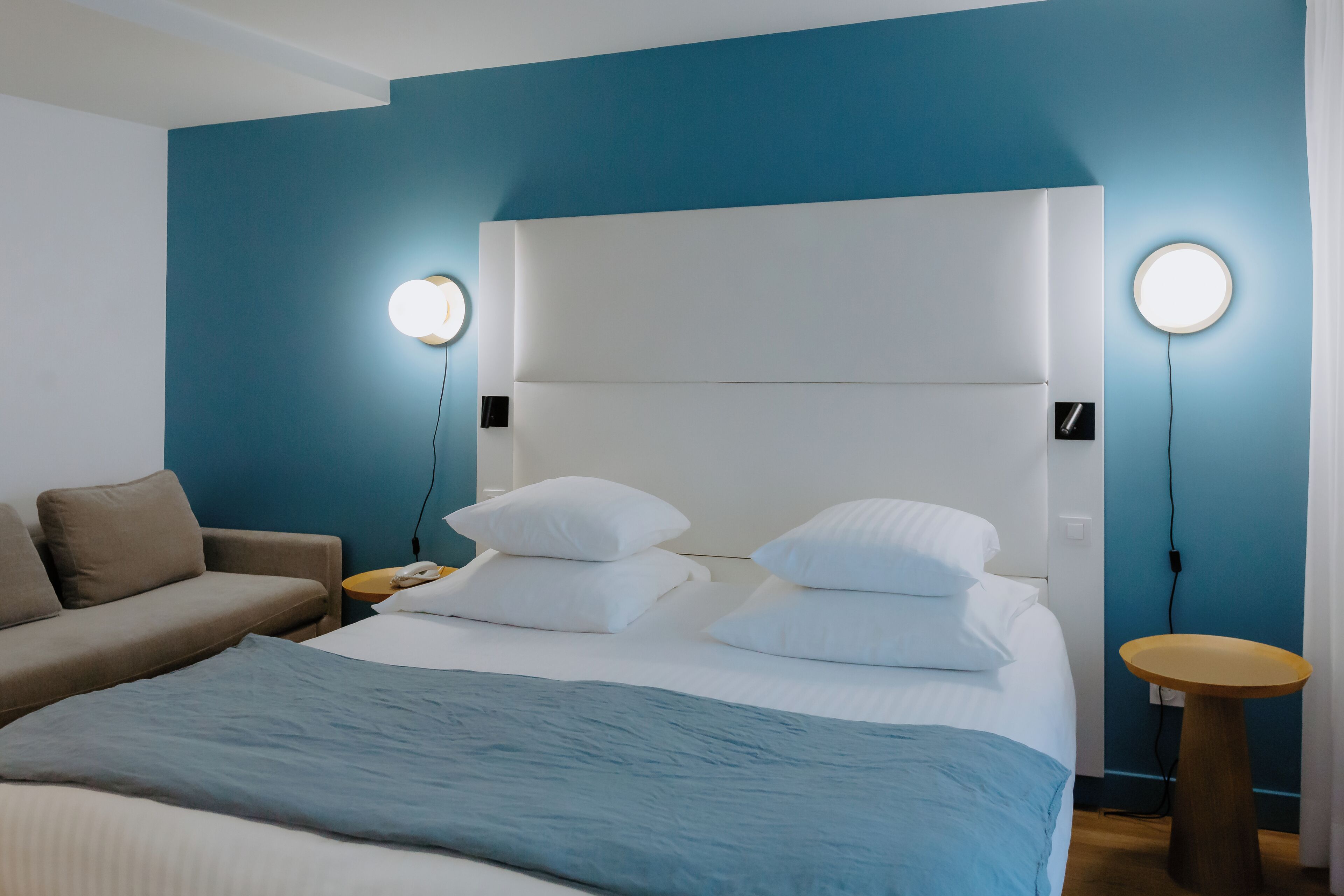 Una habitación de hotel moderna con una cama grande, un sofá y dos mesitas de noche.