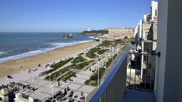 Une promenade en bord de mer, avec une plage, un phare et une rangée de bâtiments.