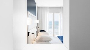 Une chambre d’hôtel moderne dotée d’une grande fenêtre, d’un lit avec du linge de lit blanc et offrant une vue sur le paysage urbain.