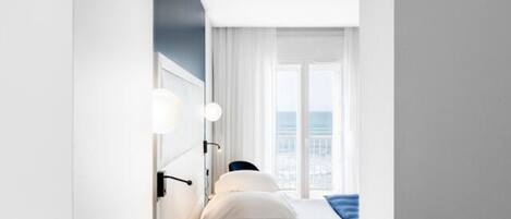 A modern hotel room with a large window, a bed with white linens, and a view of the cityscape.