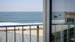 Une vue sur l’océan depuis un balcon doté d’une balustrade, avec une plage et un bâtiment au premier plan.