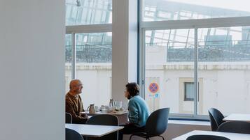 Un comedor moderno con mesas y sillas, ventanas amplias y un techo con un diseño único.