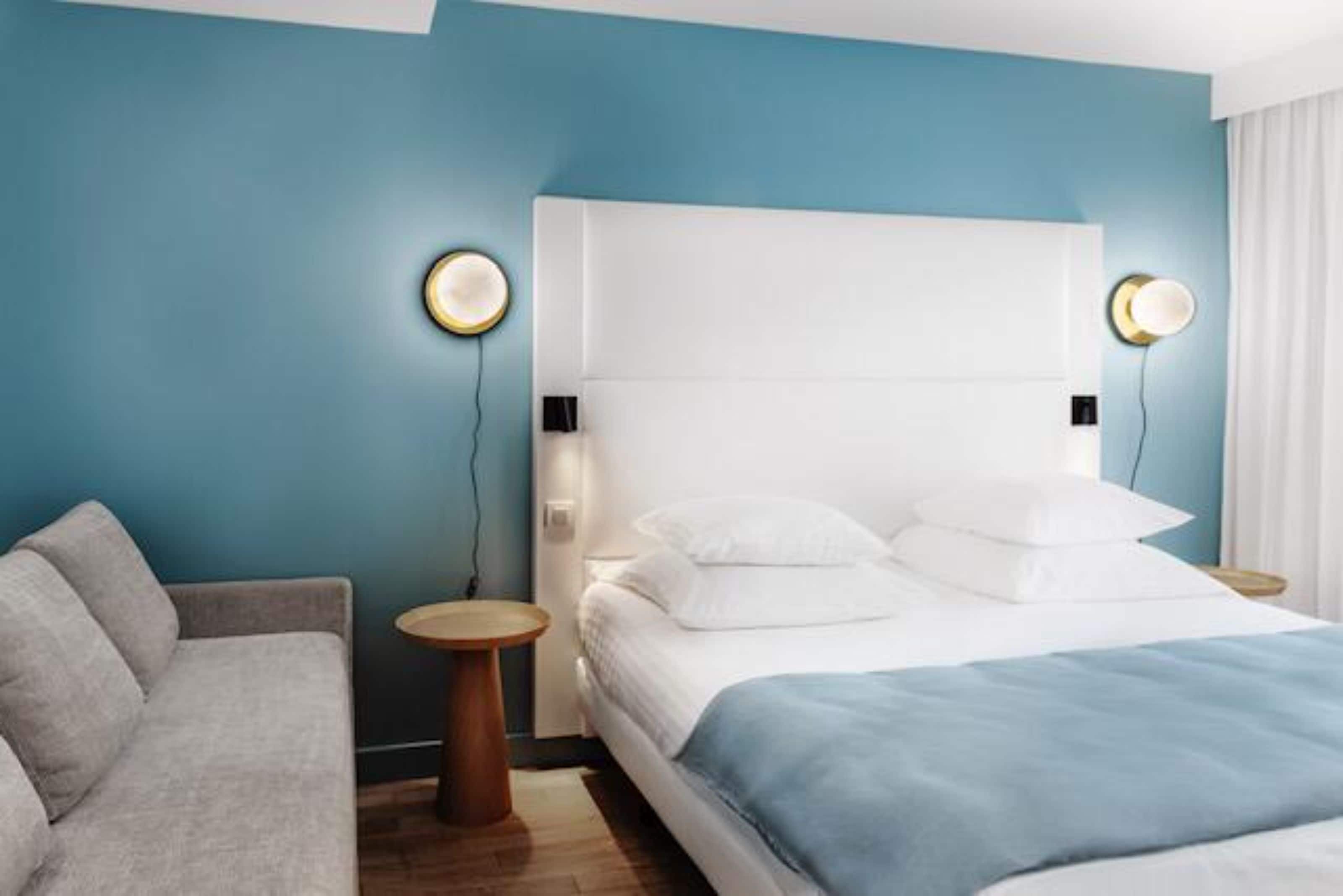 A hotel room with a bed, a sofa, and two bedside tables with lamps.