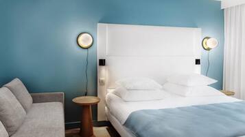 A hotel room with a bed, a sofa, and two bedside tables with lamps.