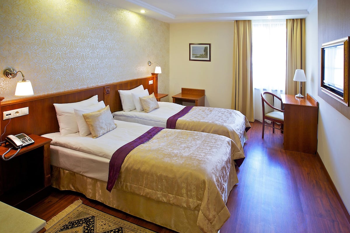 Habitación de hotel con dos camas, un escritorio, una silla, un teléfono y un cuadro en la pared.