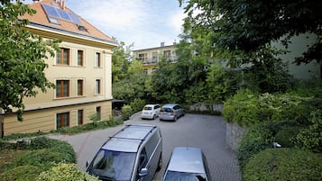 A residential area with parked cars, a building with a tiled roof, and surrounding greenery.
